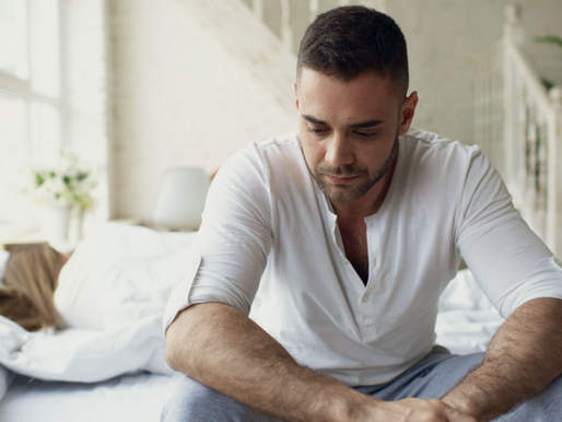 Young man sitting on the edge of a bed looking tired, illustrating symptoms that may be associated with low testosterone.