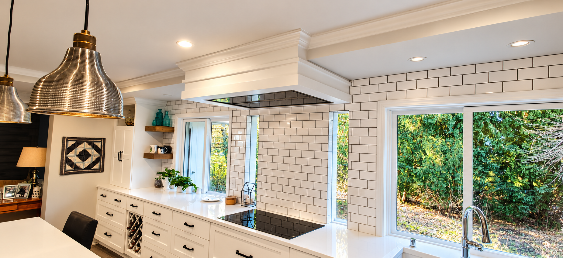 A white kitchen with a custom hood, black cooktop, and windows overlooking the garden