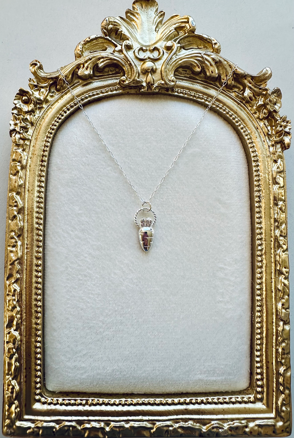 Silver carrot vegetable necklace displayed on gold ornate frame