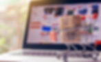 A little shopping cart with packages in front of a laptop