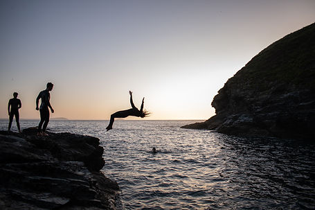 someone doing a backflip into the sea at sunset