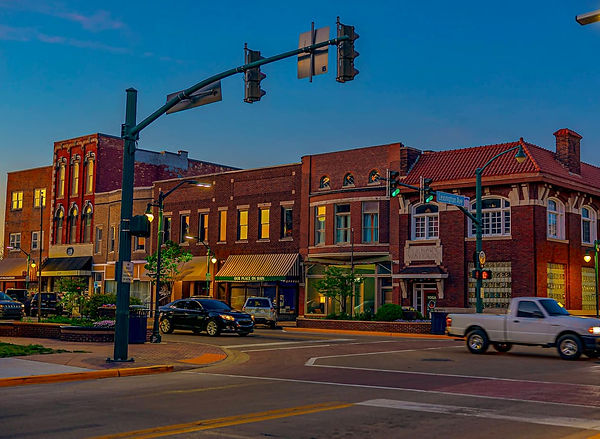 Downtown Elkhart at dusk with cars and historic brick buildings along Main Street, including the block where Elkhart Yoga Mystic is located near Lexington Avenue.