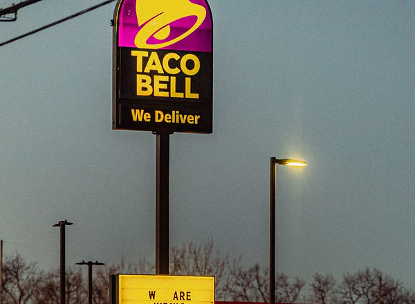 The Taco Bell sign with a dark sky and a glowing lower sign that says "we're hiring", on county road 17, in Elkhart.