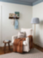 Timeless layered nursery ready for a baby boy showing a linen chair with a Swedish burnt orange blanket and floor lamp with checkered lampshade