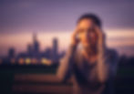 magem horizontal realista em proporção 4:3 de uma jovem adulta de cerca de 20 anos, sentada em um banco de parque ao entardecer, massageando as têmporas com uma expressão de tensão e esperança, refletindo o ciclo de alívio da enxaqueca. Ao fundo, um horizonte urbano desfocado em tons de roxo e laranja, com linhas etéreas saindo de sua cabeça simbolizando dor e esforço mental. A cena é iluminada por luz suave do fim de tarde, destacando seu rosto cansado, com uma paleta de cores que mistura roxos profundos, laranjas quentes e cinzas suaves, evocando luta e consolo. Estilo fotorealista de alta resolução com composição de ângulo amplo para conexão emocional.