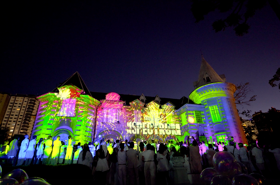 Fachada do Castelo do Batel iluminada por projeção mapeada épica da PixelSAV na festa de fim de ano da Ebanx, transição do branco puro para explosão psicodélica de cores ao pôr do sol, com fogos de artifício e rosto dos colaboradores em destaque simbolizando diversidade.