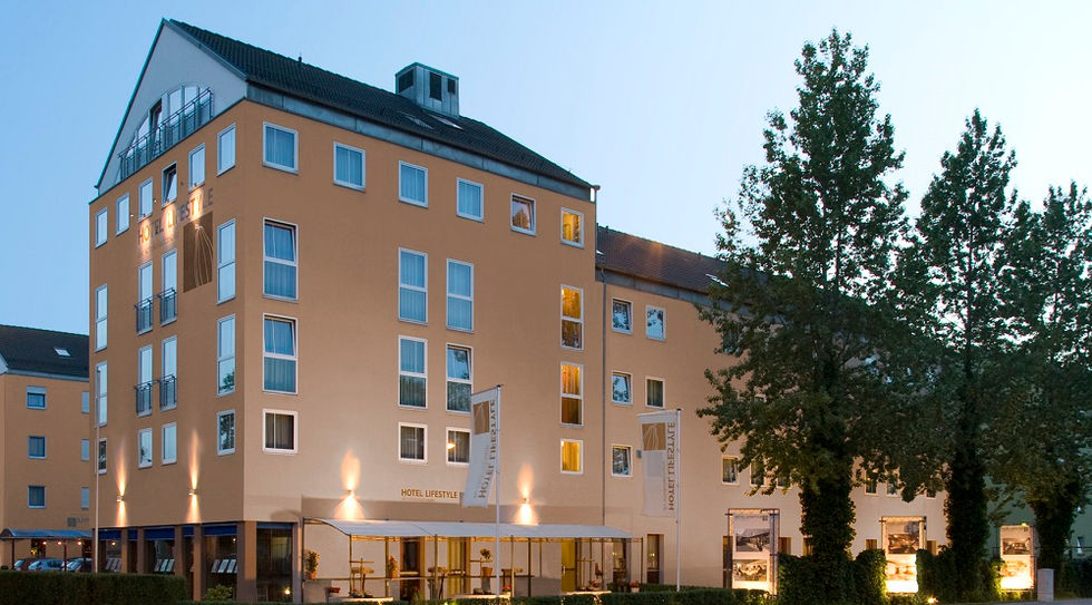 Exterior view of a multi-story hotel with illuminated windows and trees in the foreground.