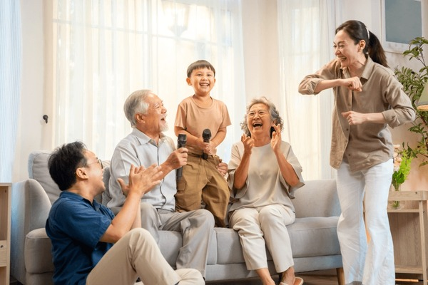 Elderly woman and nurse sharing a joyful moment, holding hands. They sit on a sofa in a cozy, well-lit room. Emphasis on companionship.