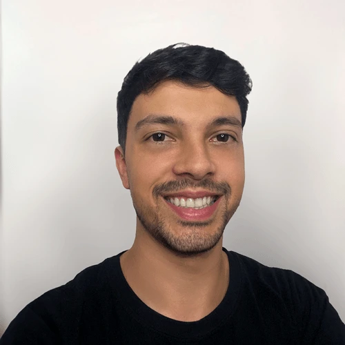 Foto de Brunno Rey, identificado como Designer, sorrindo com cabelo curto e barba discreta. Ele veste uma camisa preta e está posicionado contra um fundo branco.
