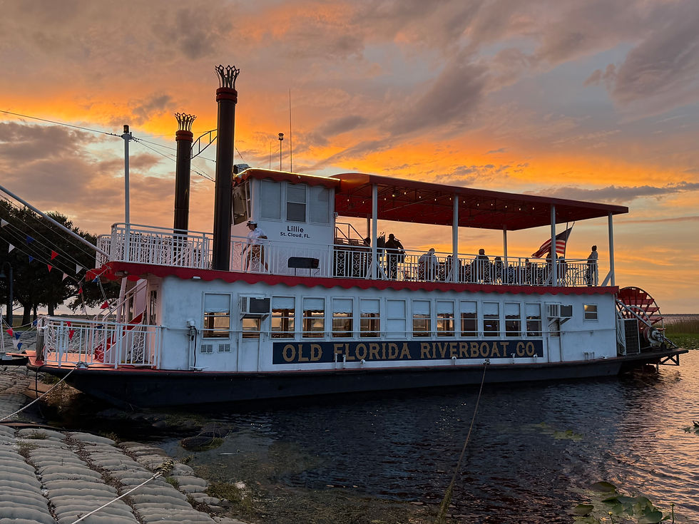 Riverboat "Lillie" docked at sunset, with people on deck. Colors of orange sky reflect on water. Text: "Old Florida Riverboat Co."