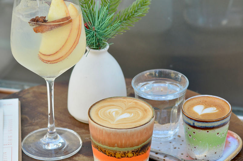 Verschiedene Kaffeesorten, Wasser und Cocktail mit Apfel auf einem Holztablett.