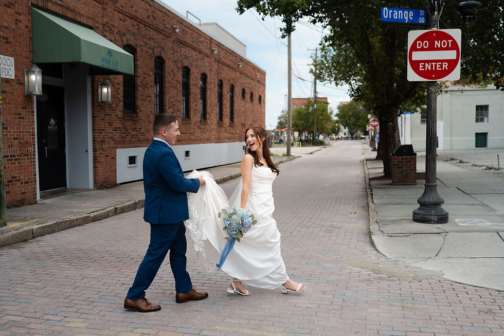 Groom carrying bride's dress train as they walk across historic downtown Wilmington NC street near 128 South