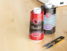 Red and black Maxi-Lock thread spools on a wooden table next to a pair of metal thread snips.