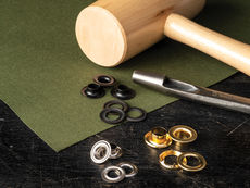 Metal grommets, a grommet inserter, and a wooden mallet on fabric