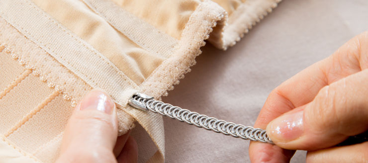 Dressmaker's hands inserting spiral metal boning into a casing on a beige corset.