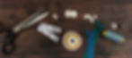 Sewing tools on a wooden table, including scissors, tape measure, thread, zippers, buttons, thimble, pins, and bobbins.