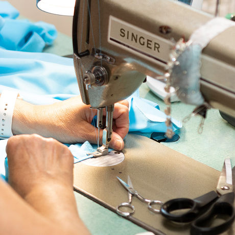 Hands sewing a hem on light blue fabric with a Singer machine.