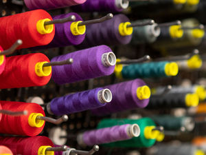 Various colors of sewing thread hang from a pegboard. Purple Gutermann threads are in focus, with various shades of red, green and gray threads blurred in the background.