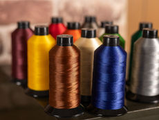Various vibrant spools of nylon bonded thread in a variety of colors. A brown and blue spool are in the foreground, with various other spools blurred behind them.