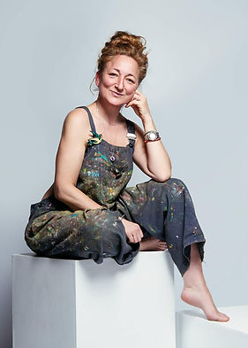 Miriam Vincent wearing paint spattered dungarees is sitting and smilling to the camera - the owner of Minnie La La Designs