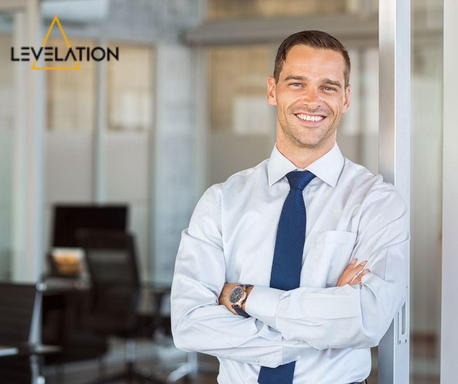 Career Starter Energiser Program - shows a man in a white shirt and blue tie leaning on a wall with a blurred image of an office behind him, he is smiling and has dark close cut hair, his arms are folded, he is in his late 20s