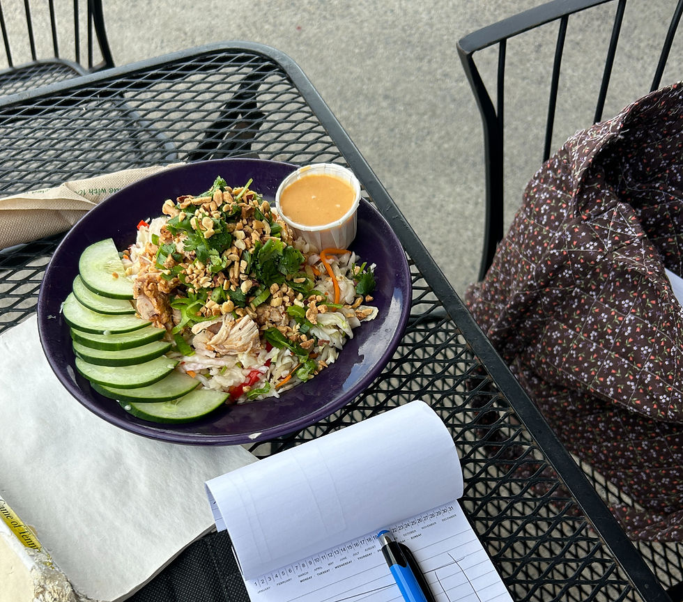 A book, a note book, and a large salad on an outdoor table