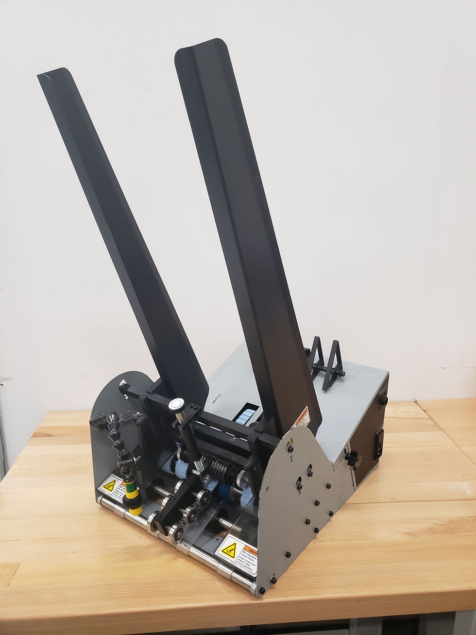 Industrial tabletop friction feeder machine with two vertical black guide rails and metal construction, placed on a wooden surface