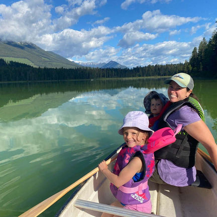 A mom with her two children in a canoe on a calm lake with mountains in the background.