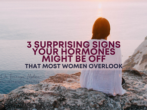 Woman in white sits on rocky cliff at sunset overlooking sea. Text reads: 3 surprising signs your hormones might be off that most women overlook.