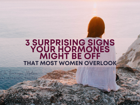 Woman in white sits on rocky cliff at sunset overlooking sea. Text reads: 3 surprising signs your hormones might be off that most women overlook.