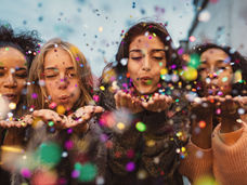 Group of women celebrating the New Year together, blowing confetti and embracing joy, connection, and new beginnings