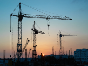 Silhouettes of multiple tower cranes at a construction site against a sunset sky.