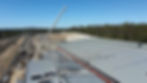 An aerial view of a construction site with a crane lifting large roofing panels onto a building.