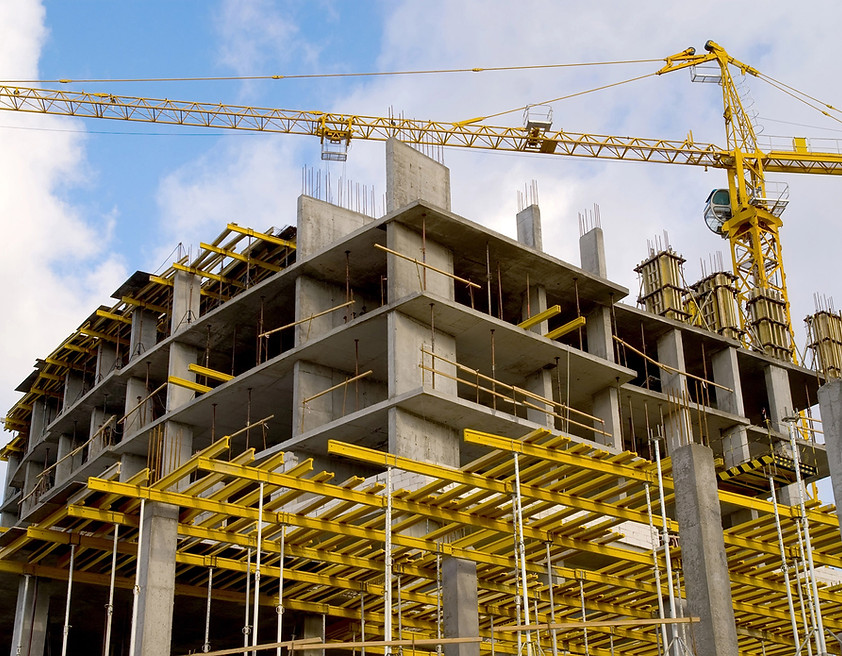 Partially constructed concrete building with yellow scaffolding and a tower crane under a partly cloudy sky.