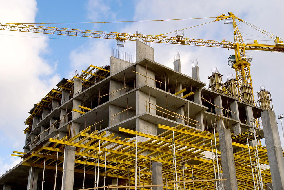 Partially constructed concrete building with yellow scaffolding and a tower crane under a partly cloudy sky.