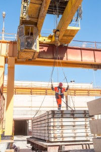 A crane operator standing on a pallet of materials being lifted by an overhead crane.