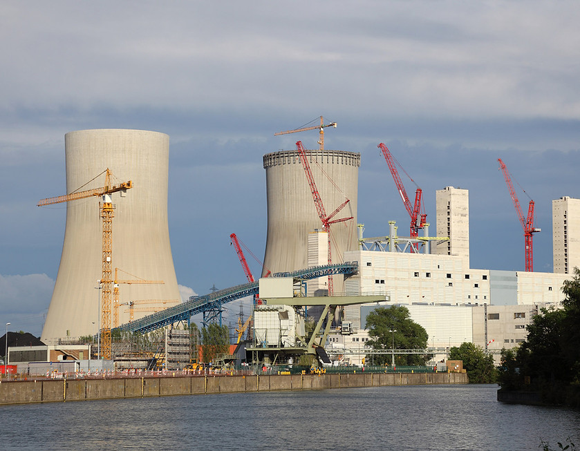 Energy facility under construction with cooling towers, cranes, and industrial buildings near a waterway.
