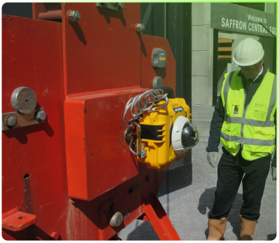 A construction worker inspects a red lifting assembly equipped with a mounted yellow HoistCam camera outside a building.