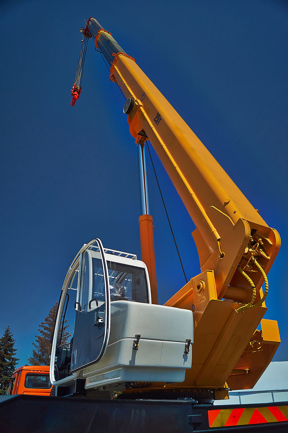 A close-up of a large yellow telescopic boom crane with its cab and red hook against a deep blue sky.