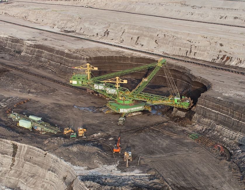 Large open-pit mining operation with excavators, conveyor belts, and layered earth formations.