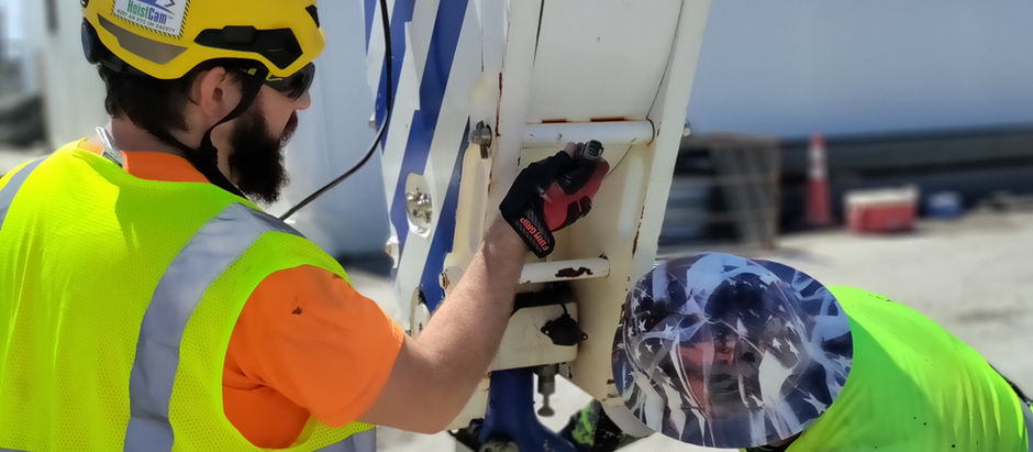 Two construction workers wearing safety vests and hard hats, attaching a chain to a crane hook block.
