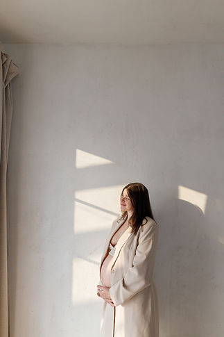 Stylish beautiful pregnant woman in beige suit holding baby bump and posing against wall i