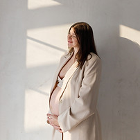 Stylish beautiful pregnant woman in beige suit holding baby bump and posing against wall i