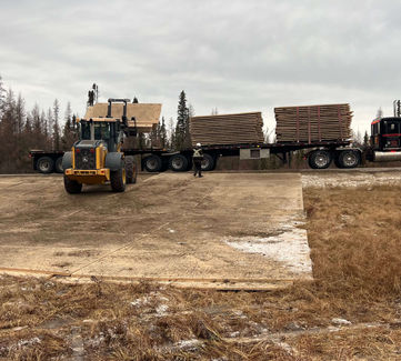Recharged Industries forklift unloading wooden mats from a semi-trailer on a cleared site, prepping for installation.