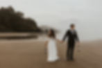 Elegant bride and groom walking hand-in-hand along a misty beach, with the groom holding a lantern, in a serene and romantic wedding scene.