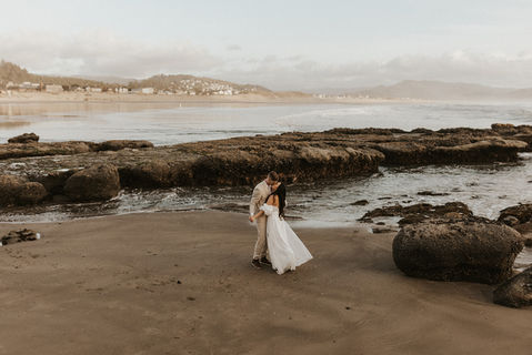 Bride and groom standing by the ocean with views of coastal rocks in Alberta
