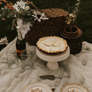 Elegant picnic setup with apple pie, flowers, and champagne in a serene park setting.