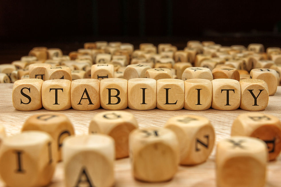 Wooden letter tiles spelling out 'stability', set apart from a scattered pile of blank letter tiles in the background.