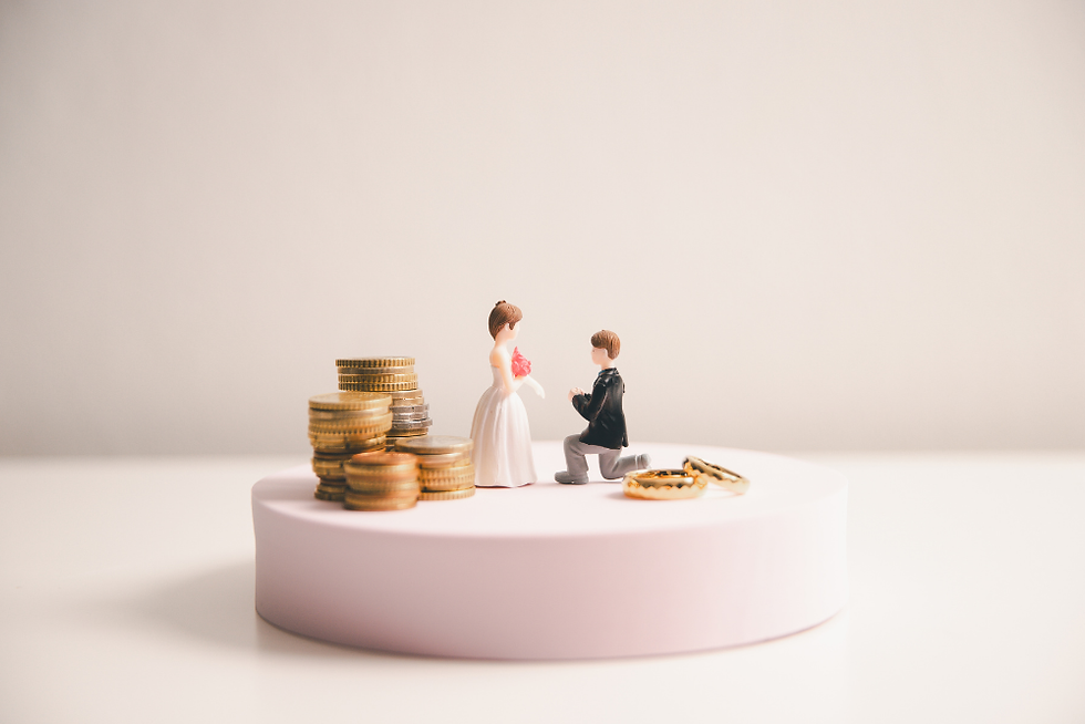 Wedding cake toppers of a bride and groom kneeling with a stack of coins and rings on a pink pedestal, symbolizing marriage and finance.