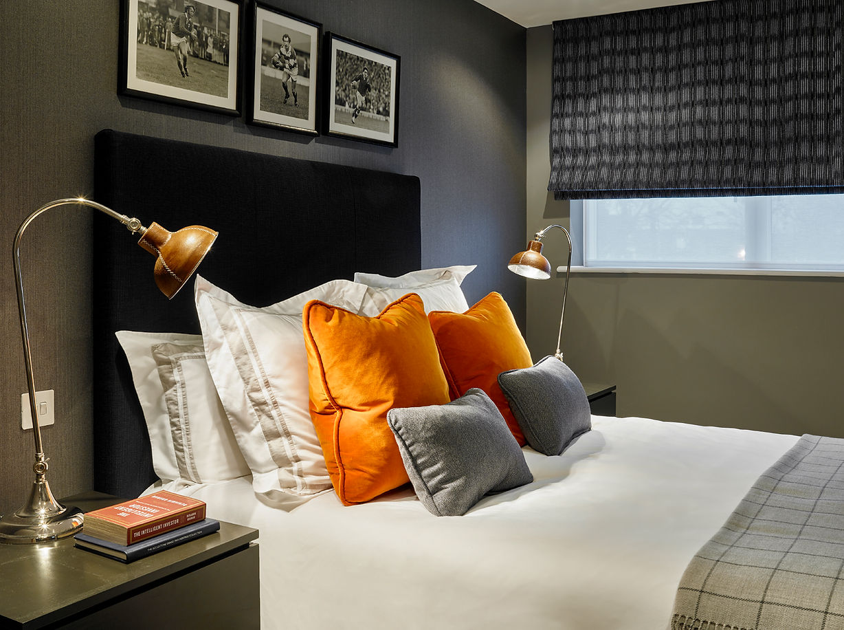 Contemporary bedroom with dark headboard, orange accent cushions and brass reading lights